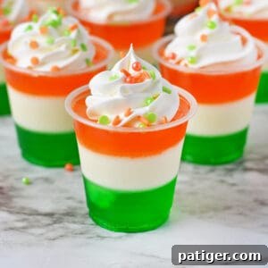 Festive St. Patrick's Day jello shots made with layers of green, white, and orange jello and topped with whipped cream and green and orange sprinkles.