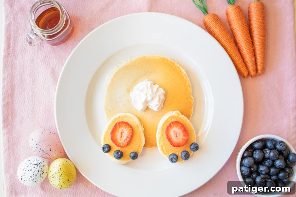Cottontail Pancakes 2 Bunny butt pancakes on white plate on pink linen with syrup, blueberries, and easter decorations around them.