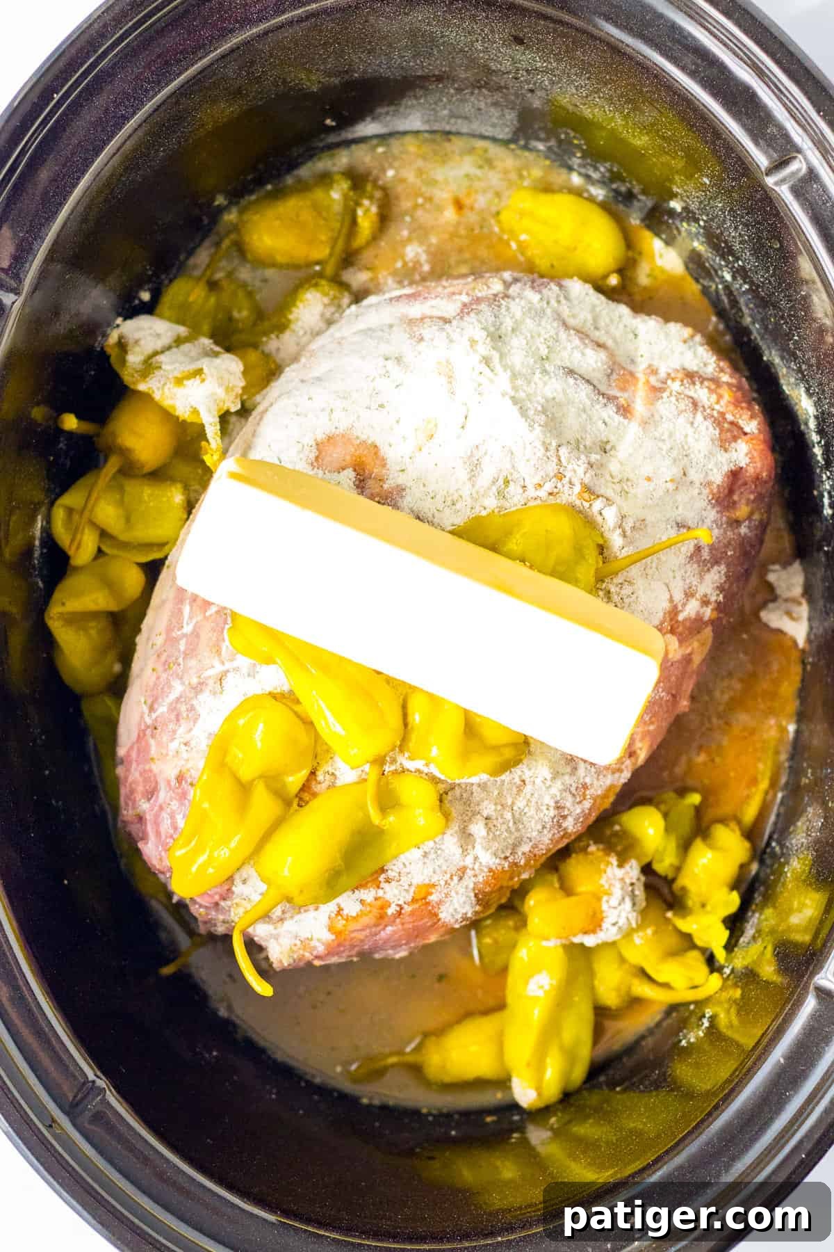 Roast in crockpot topped with seasonings, peppers, and stick of butter, ready for slow cooking.