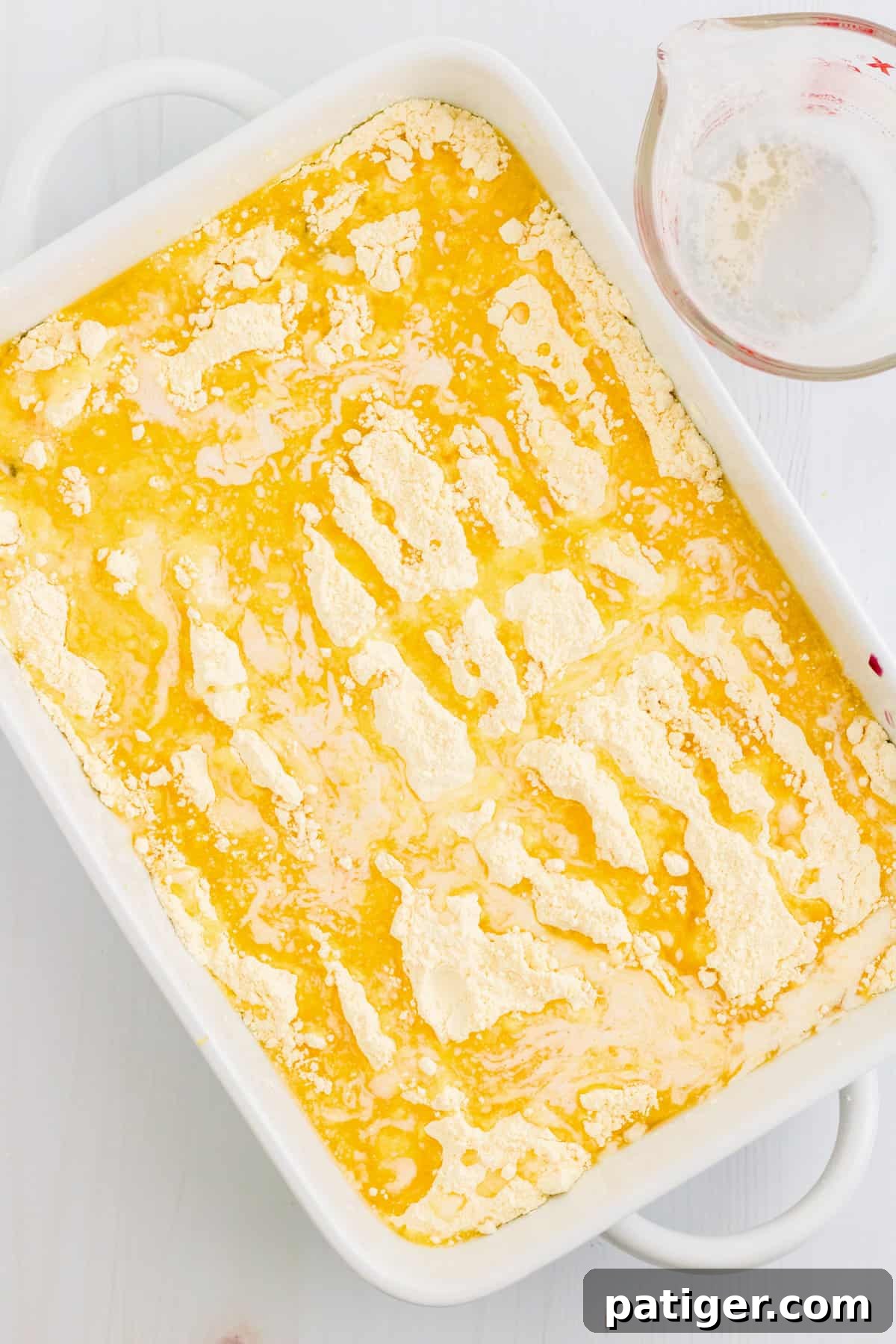 Melted butter has been drizzled generously over the dry cake mix, with a few small dry spots remaining, which is typical for dump cakes.