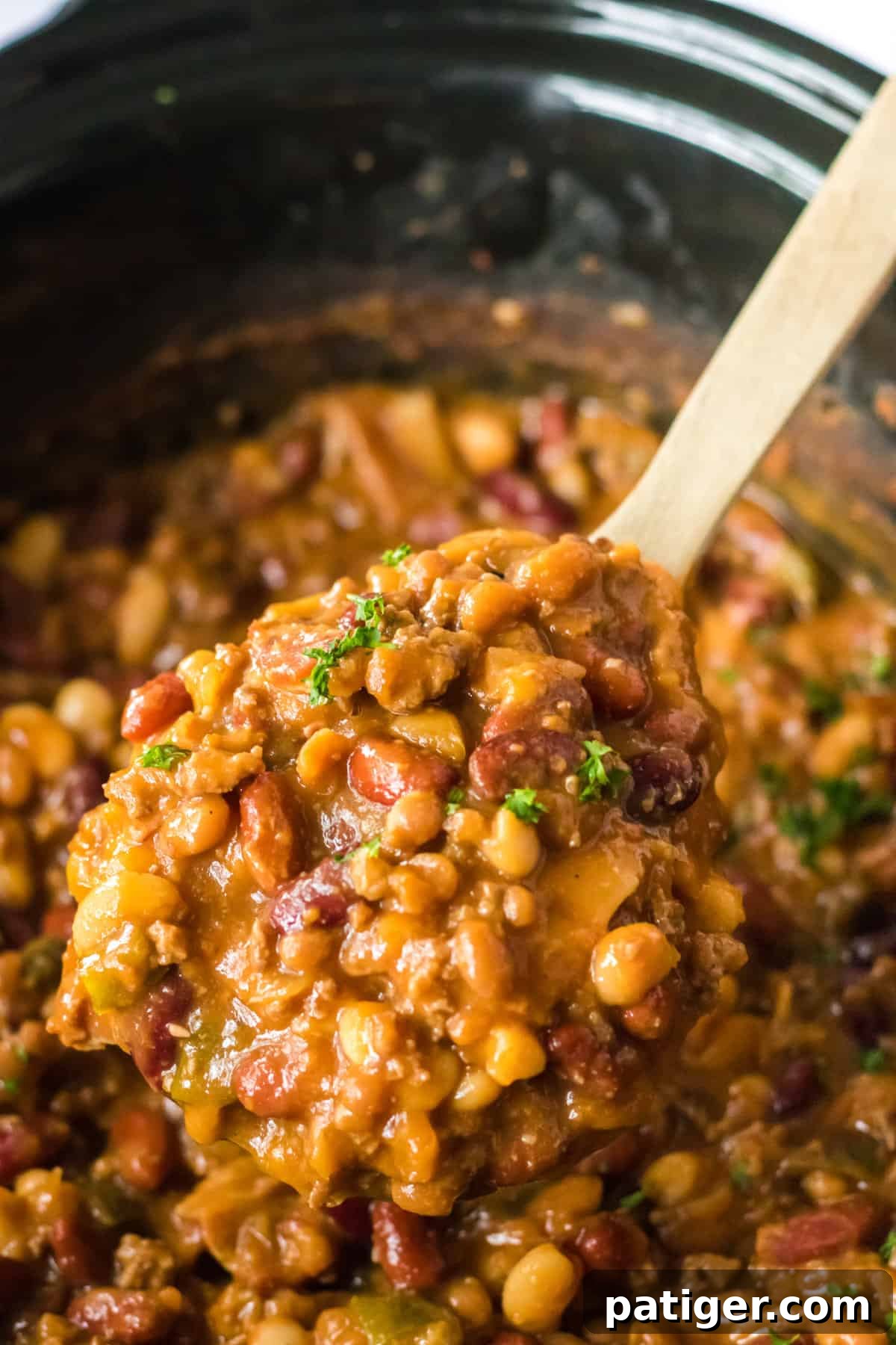 Wooden spoon lifting cowboy beans out from crockpot.
