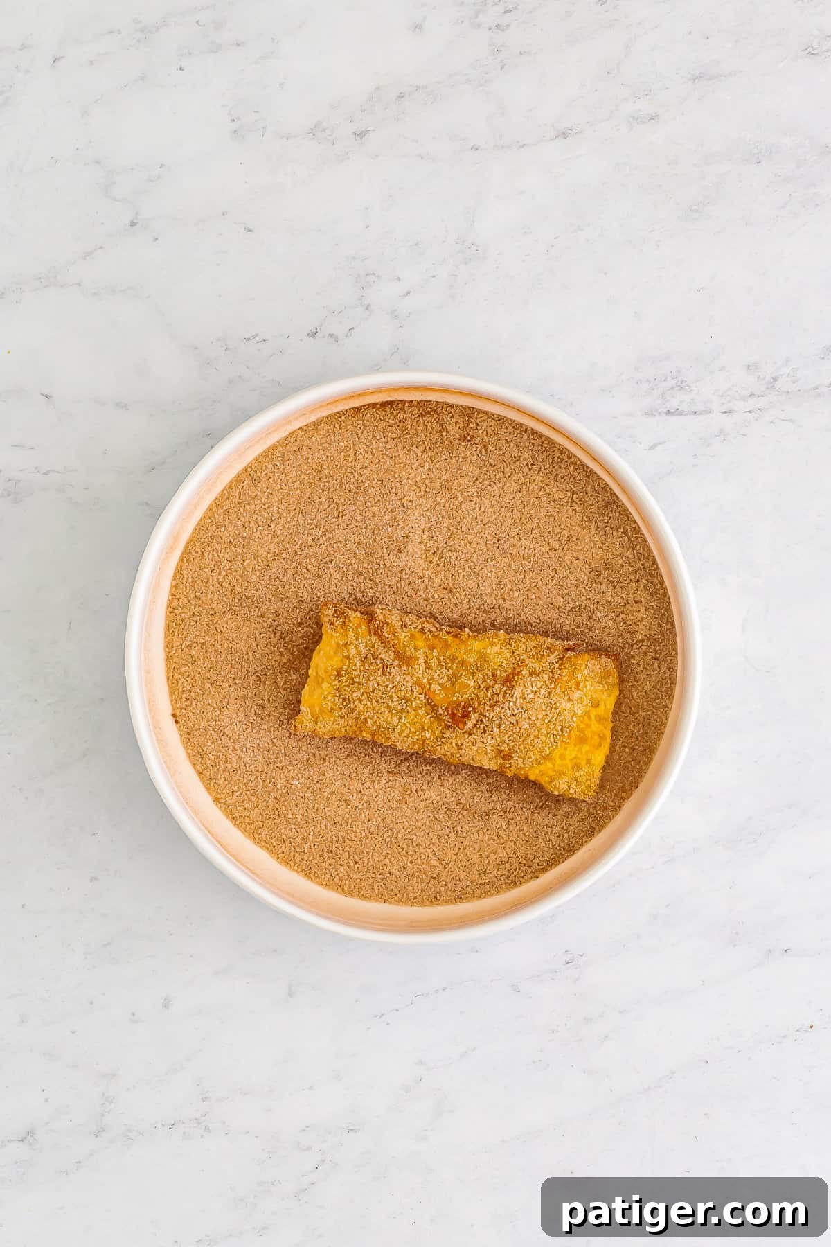 Egg roll being dipped in cinnamon sugar.