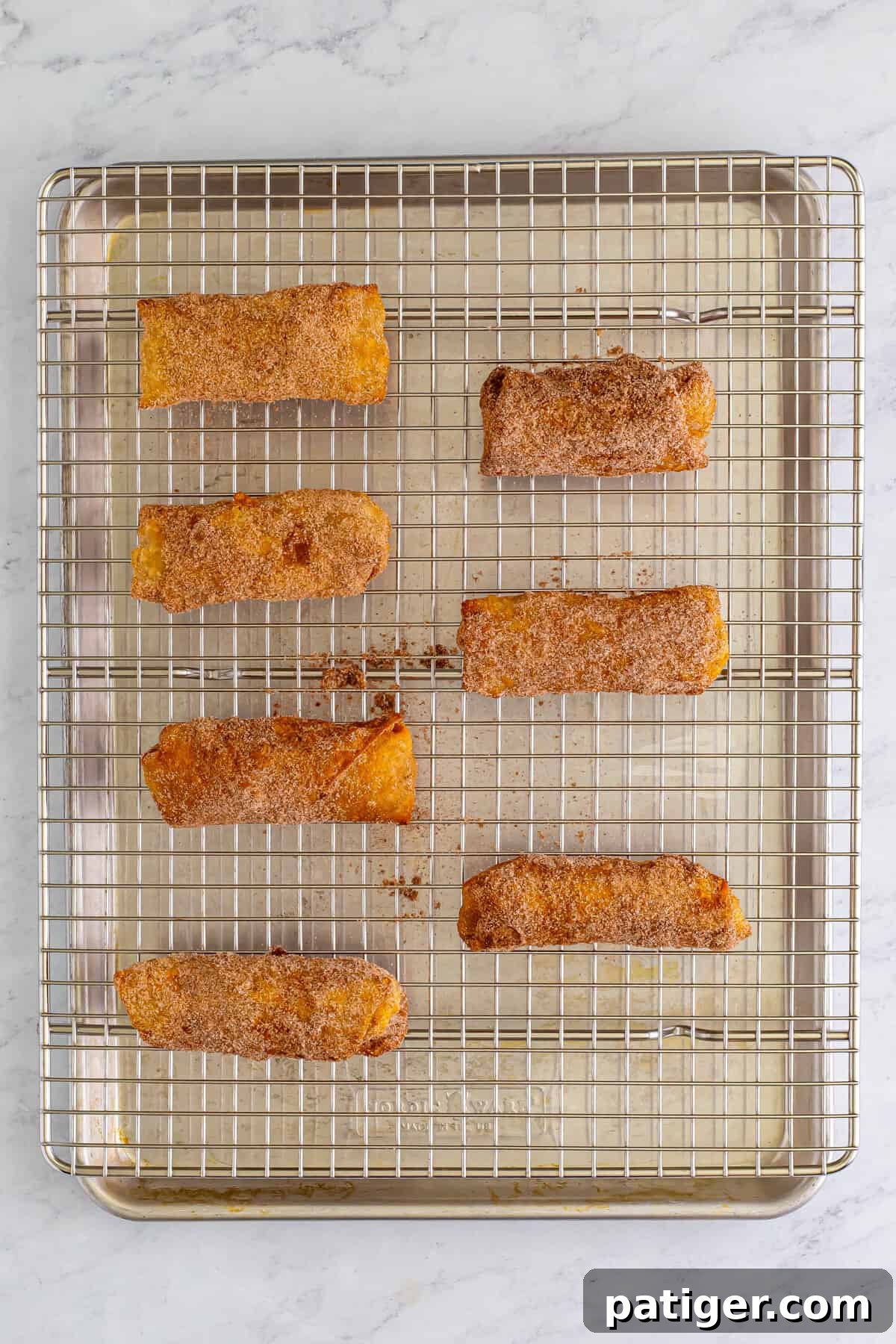 Cinnamon sugar coated egg rolls on baking sheet topped with wire rack.