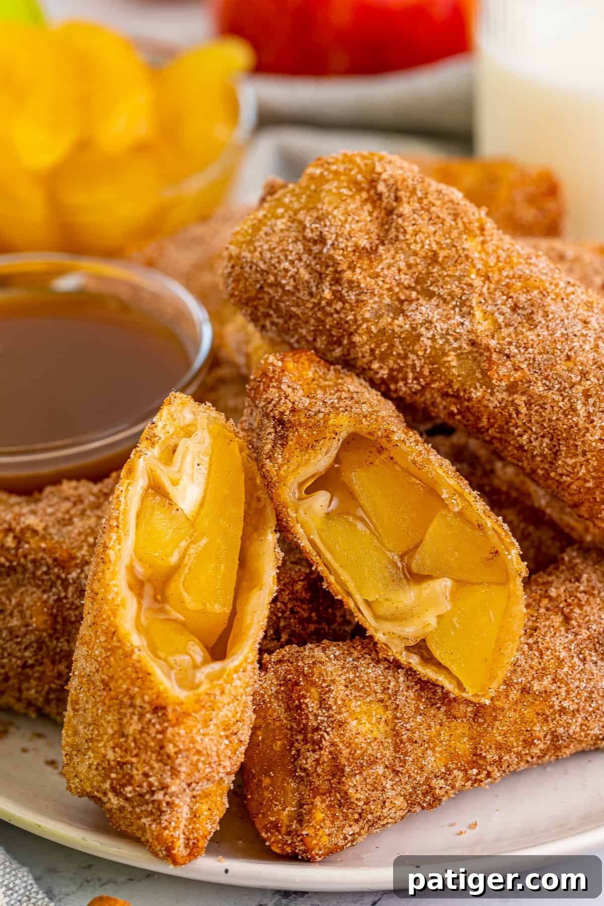 Apple pie egg rolls coated in cinnamon sugar and served with caramel sauce for dipping. One egg roll is cut in half to show apple pie filling.
