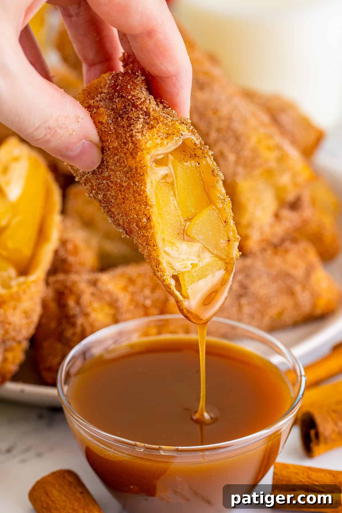 Apple pie egg roll being dipped in caramel sauce.