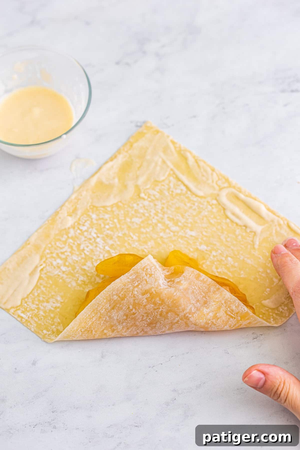 Bottom of egg roll wrapper folded up and flour paste rubbed with finger onto perimeter of wrapper.