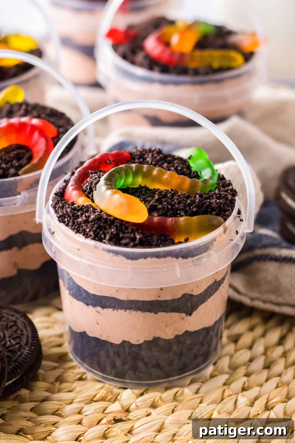 Dirt and worms pudding cups in clear pails with layers of creamy chocolate pudding and crushed oreo pieces.