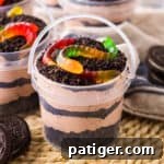 Dirt and worms pudding cups in clear pails with layers of creamy chocolate pudding and crushed oreo pieces.