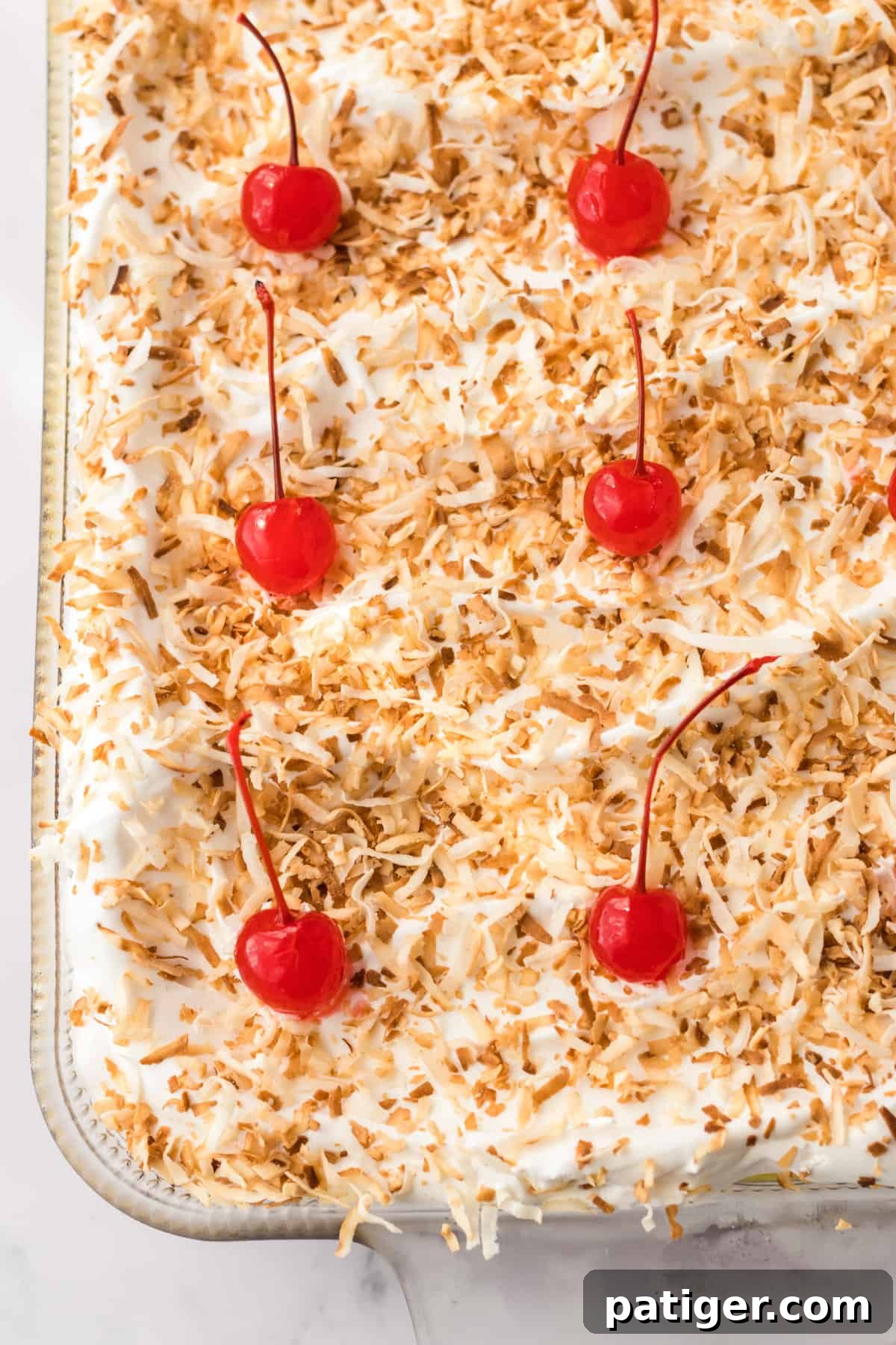 A stunning shot of the Pineapple Coconut dessert, beautifully topped with toasted shredded coconut and bright red cherries.