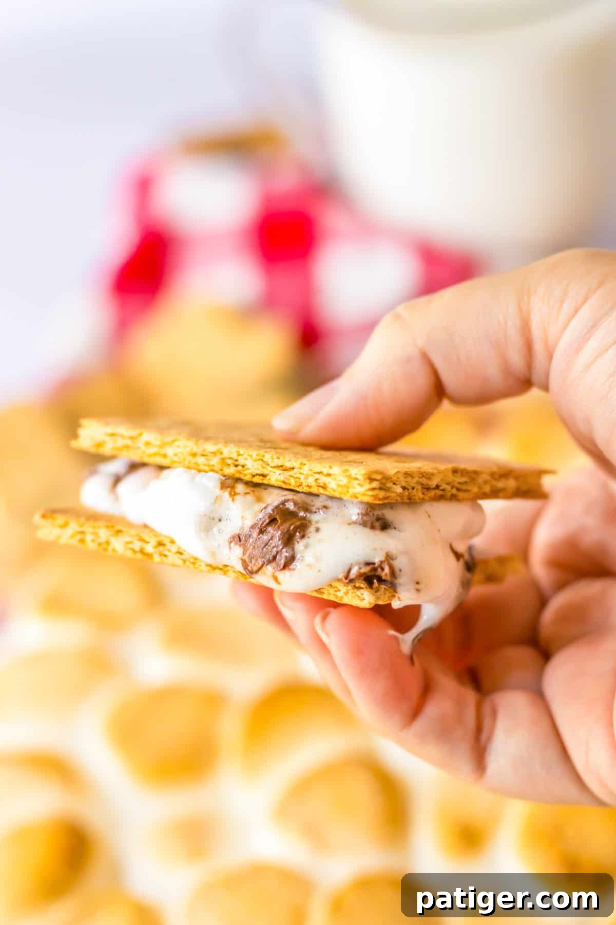 A hand holding a graham cracker sandwich, filled with warm, melted s'mores dip, demonstrating the perfect bite.