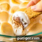 Graham cracker being dipped in s'mores dip made with marshmallows and chocolate chips.