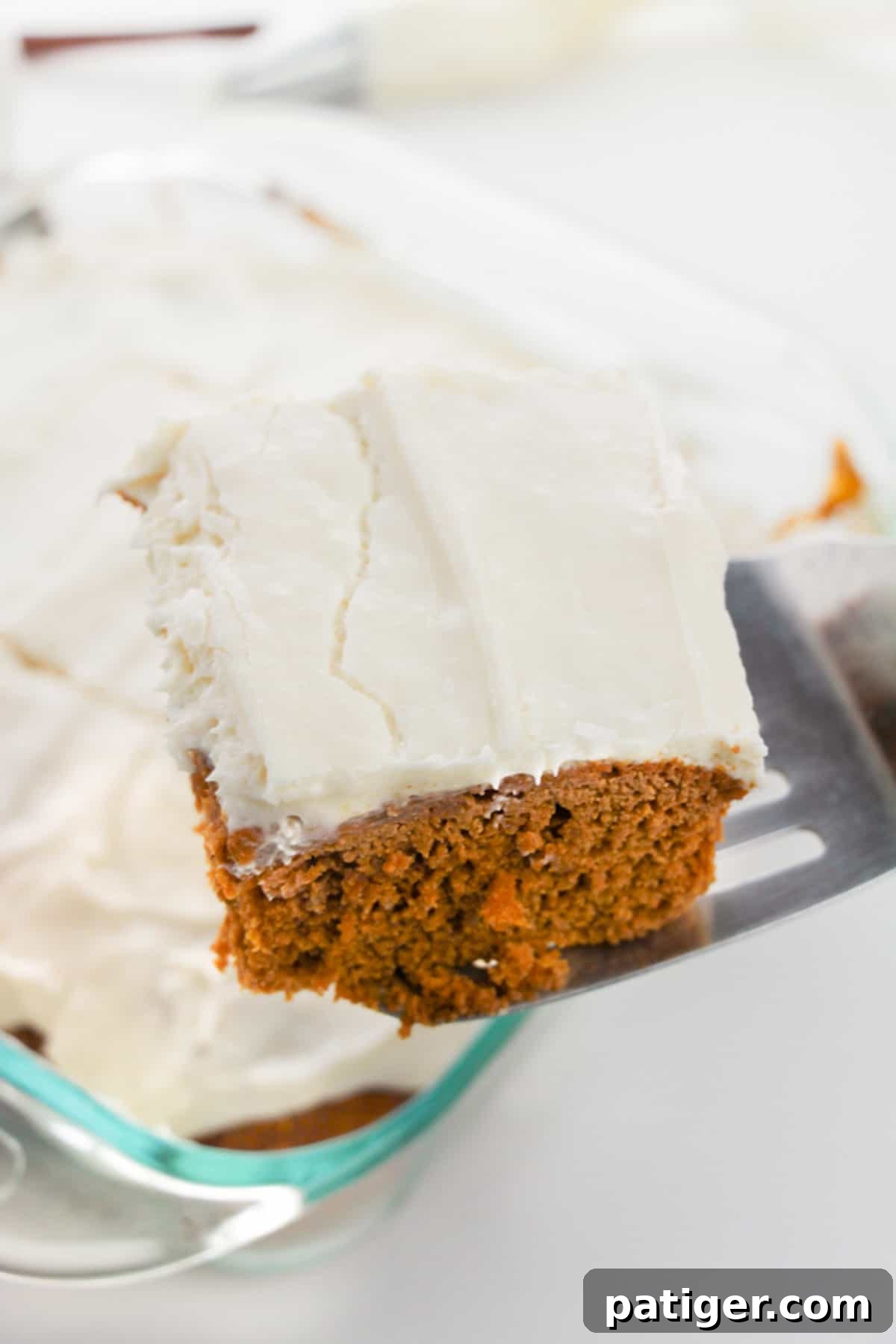 Spatula serving a piece of pumpkin spice cake from a square baking pan.