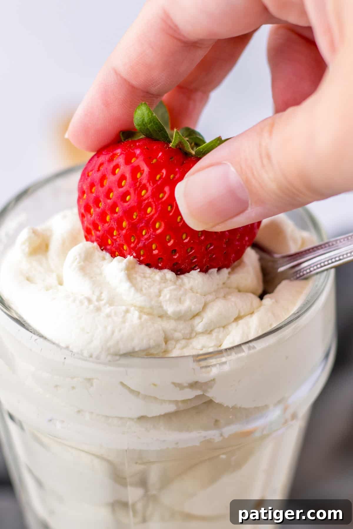 A fresh strawberry being dipped into a bowl of luscious homemade cool whip.