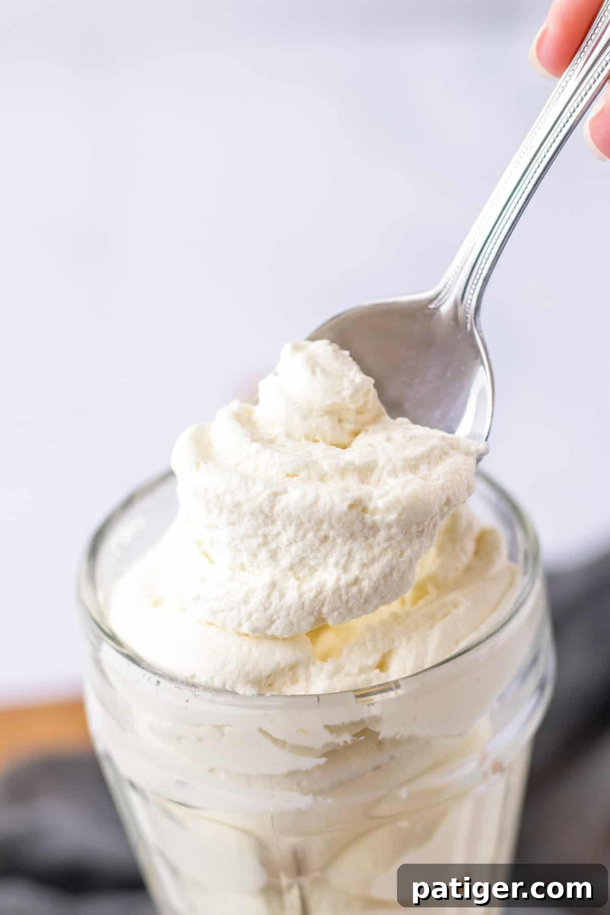 Homemade whipped topping being spooned out of a glass, highlighting its light and airy texture.