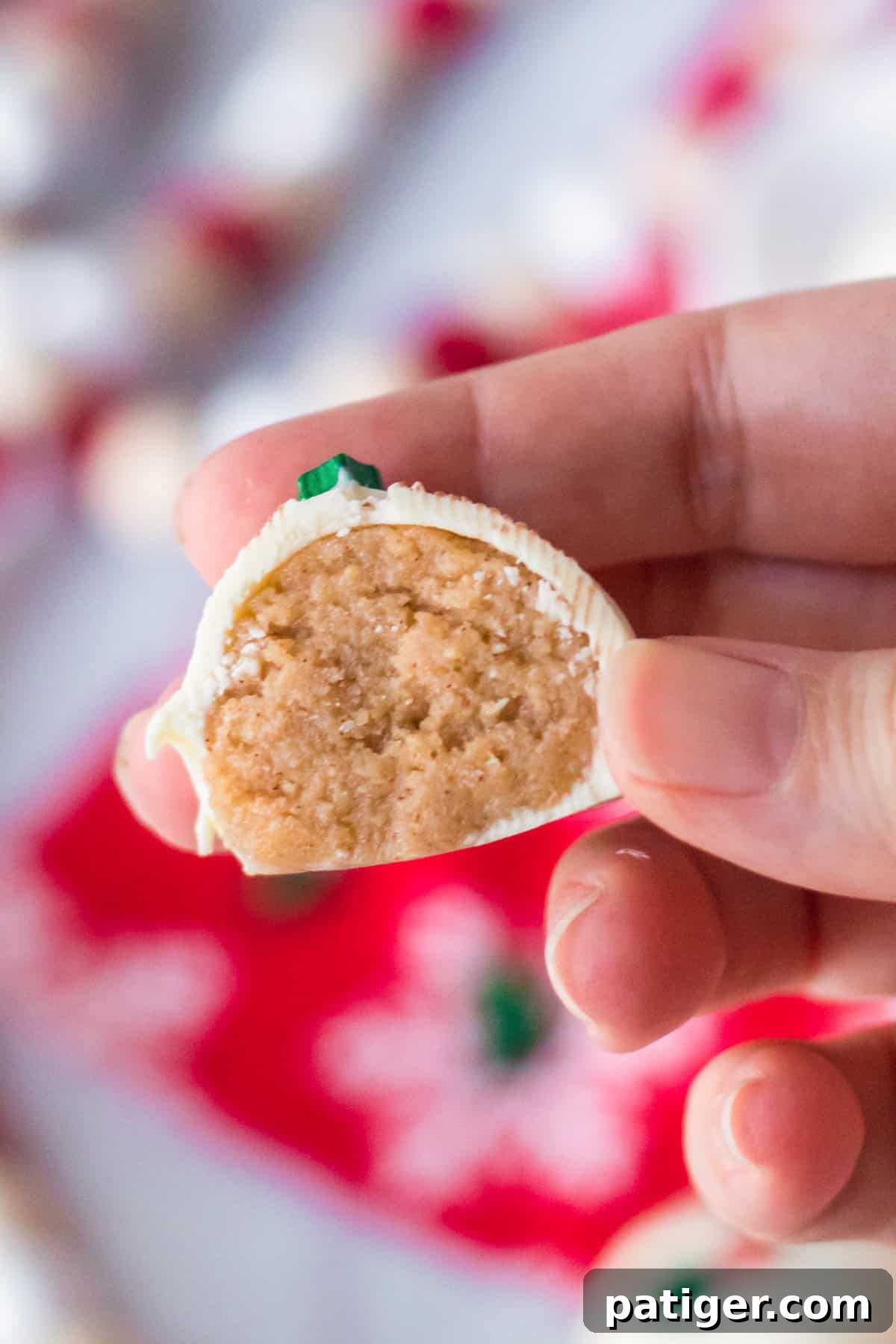 Hand holding snickerdoodle cookie dough truffle cut in half to show golden cookie mixture inside.