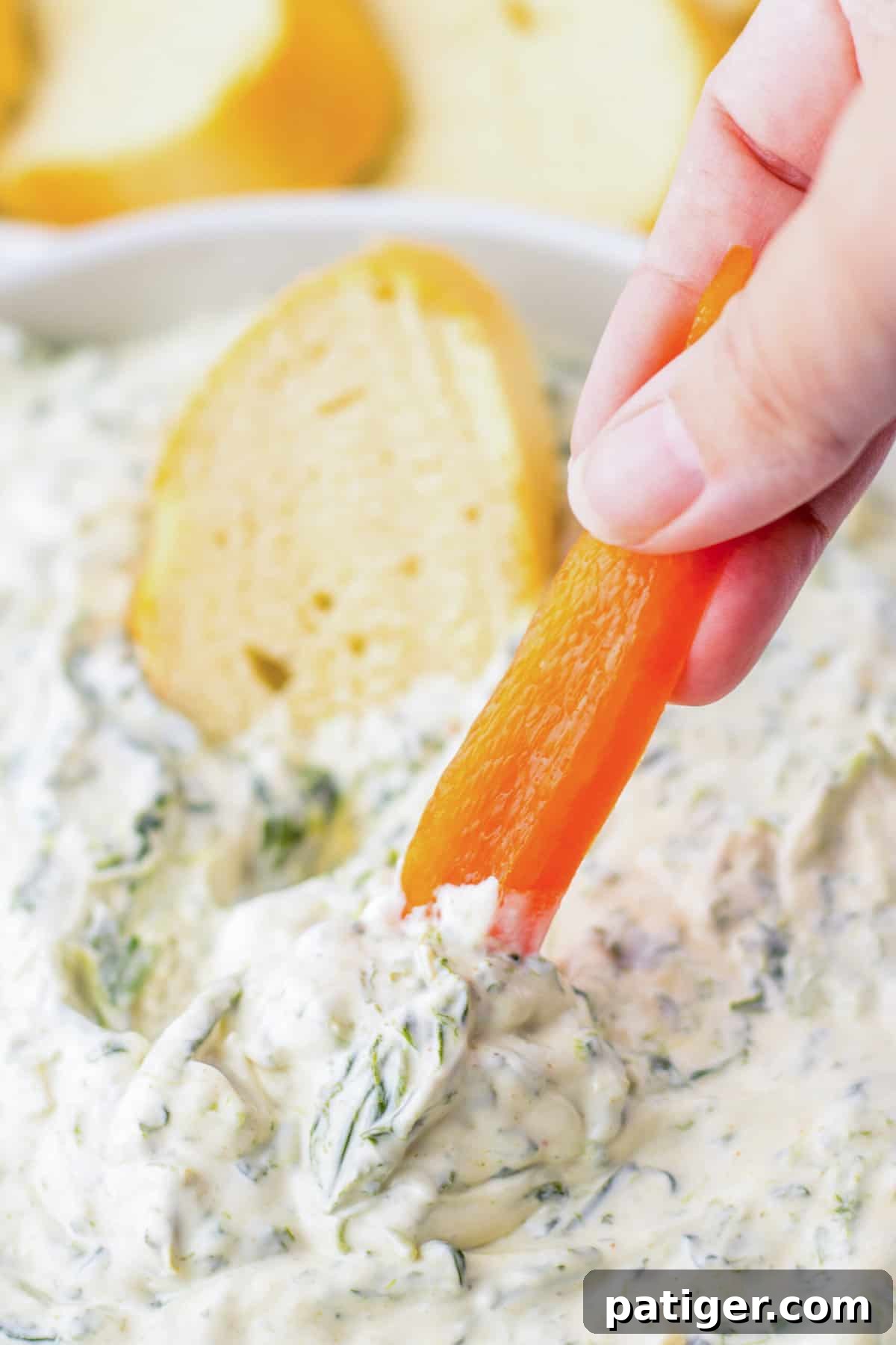 Piece of red bell pepper being dipped into spinach dip. 