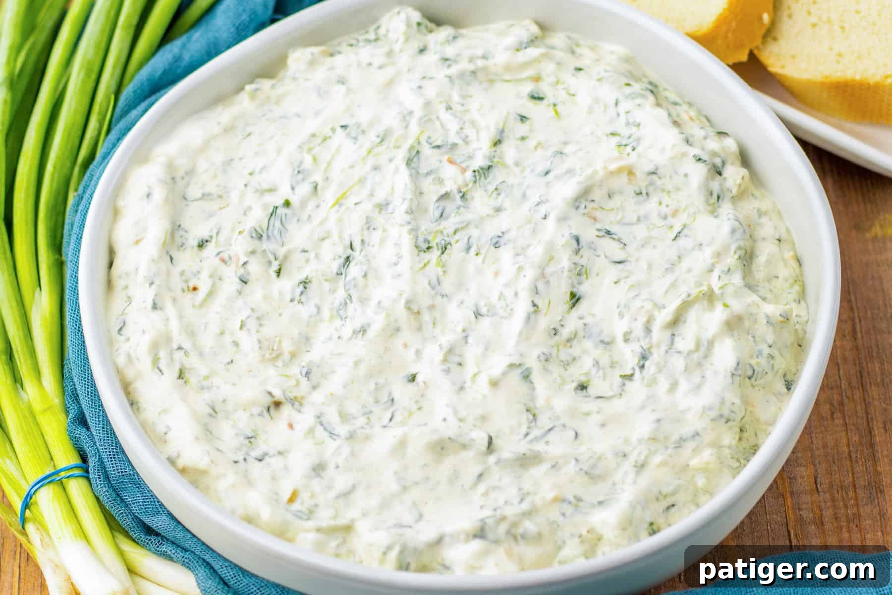 Classic knorr spinach dip with water chesnuts in white bowl with bundle of green onions beside it.