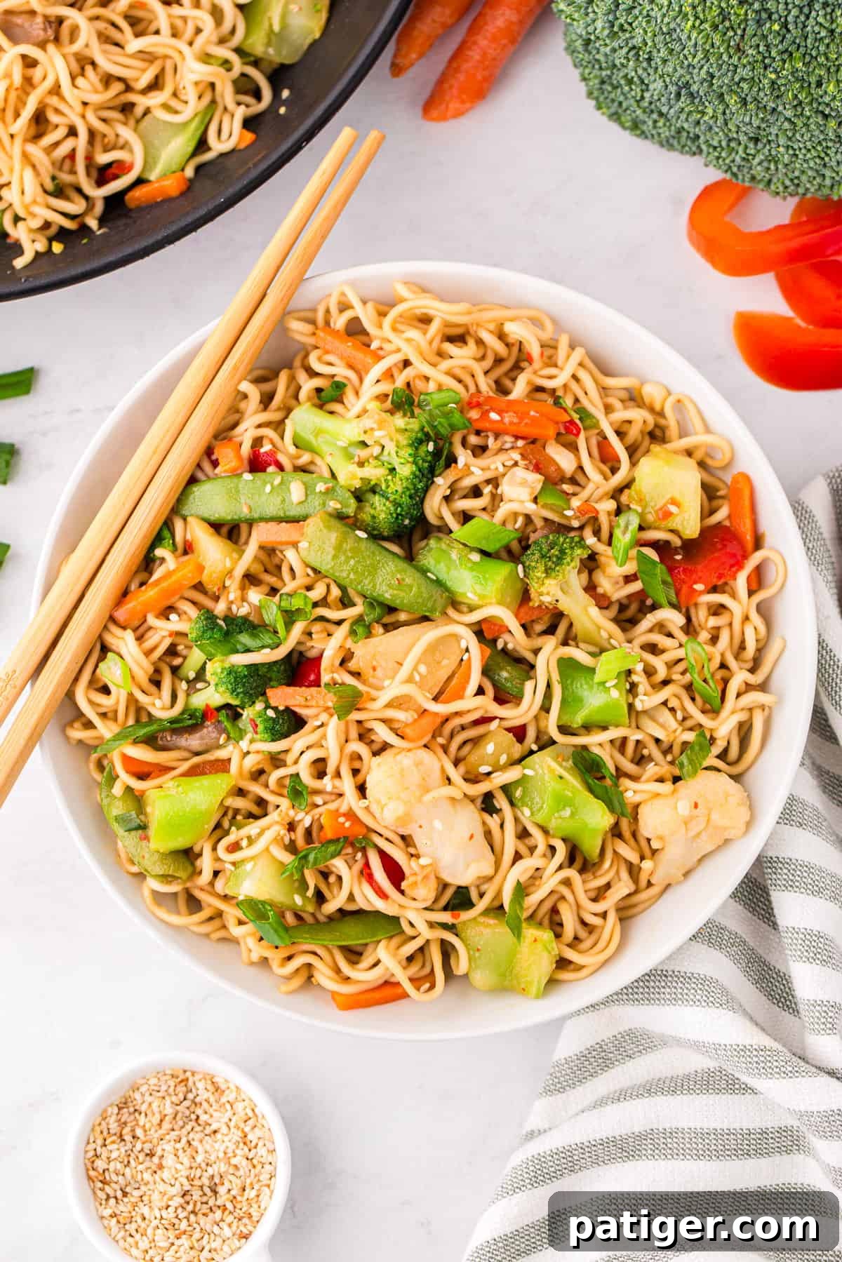 Vibrant ramen stir fry with broccoli, snap peas, carrots, bell peppers, cauliflower, mushrooms, sesame seeds, and green onions served in a large bowl with chopsticks, ready to eat.