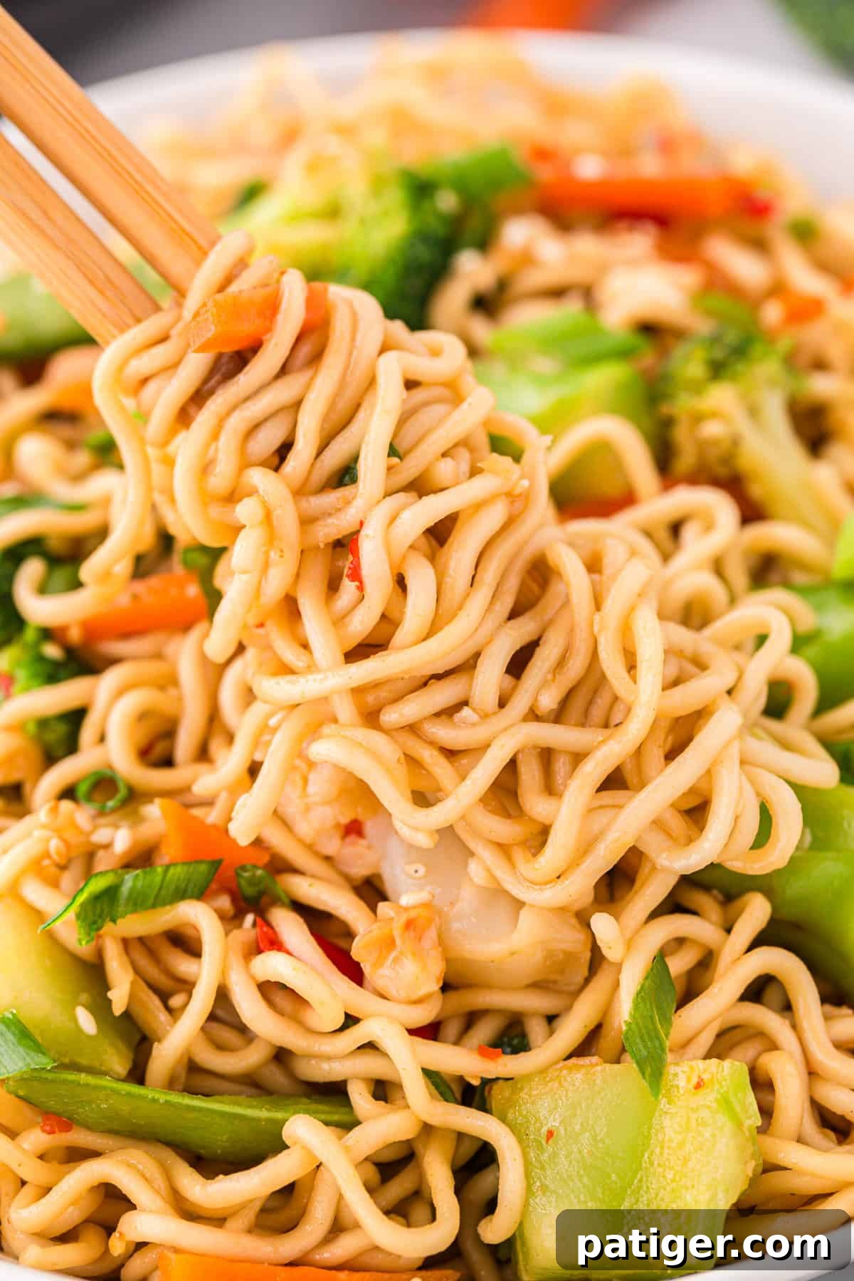 Close-up shot of ramen noodles gracefully wrapped around chopsticks, being lifted from a steaming bowl of stir-fry, highlighting their perfect texture and readiness to be enjoyed.