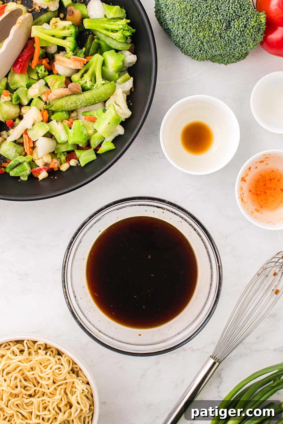 A rich, dark brown stir-fry sauce is perfectly blended in a small glass bowl, ready to be added to the dish. It is surrounded by the other fresh ingredients required for the stir fry, neatly arranged on a clean countertop.