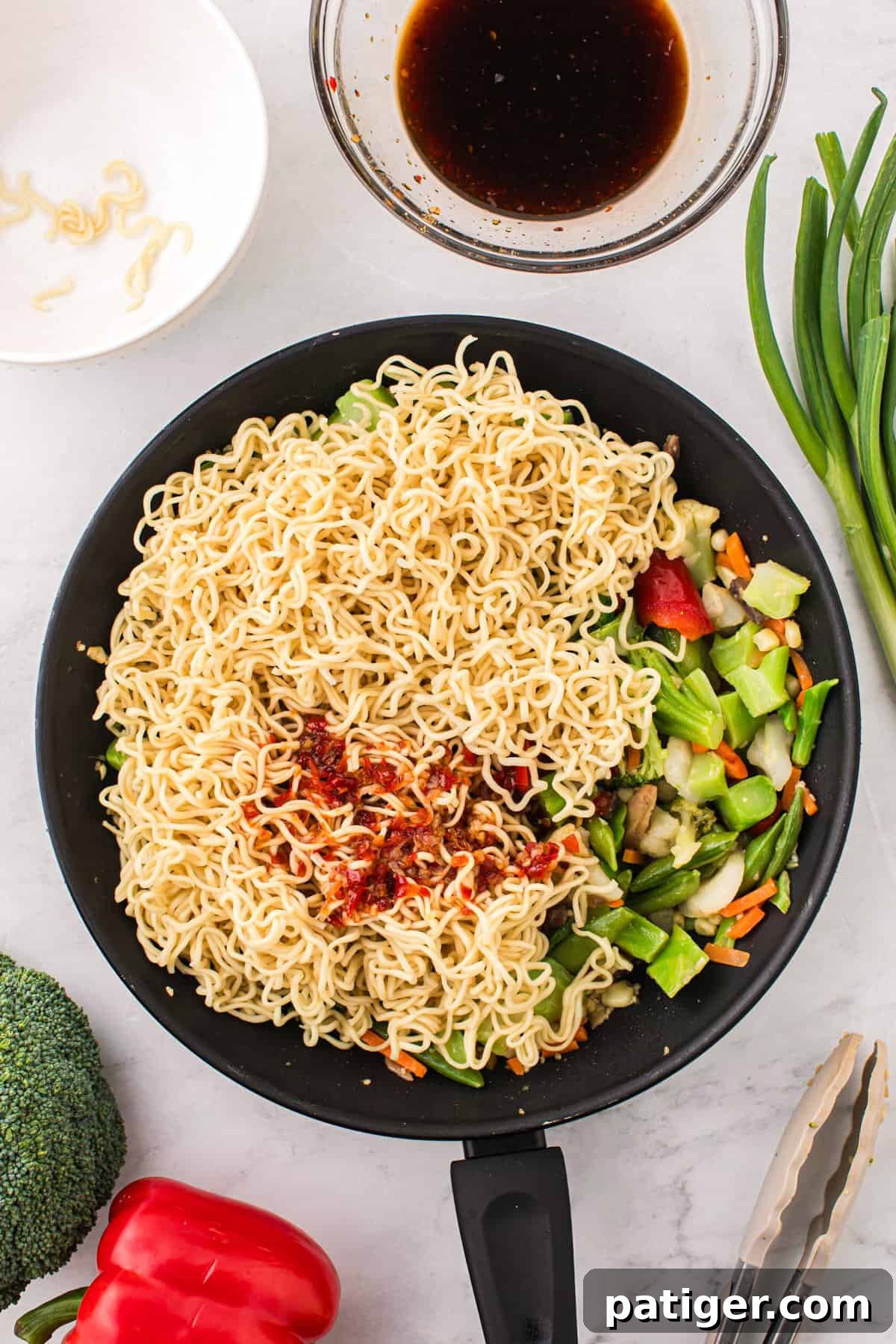 Perfectly cooked ramen noodles and a generous portion of stir-fry sauce have been added to the pan, mingling beautifully with the colorful vegetables, creating an appetizing and fully combined dish.