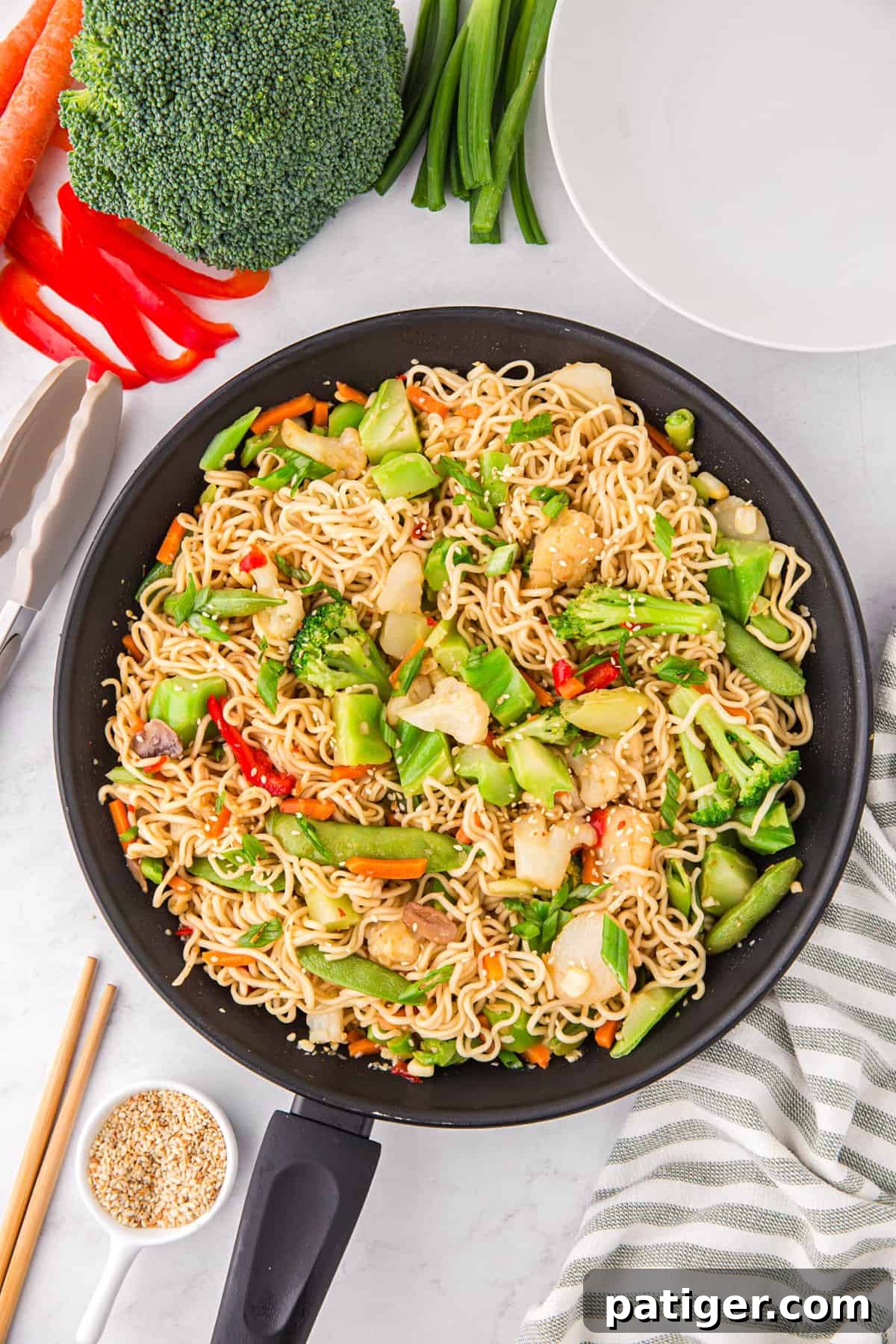 A delicious ramen noodle stir fry with a vibrant medley of colorful vegetables, perfectly cooked and beautifully presented in a sleek black pan, ready for serving.