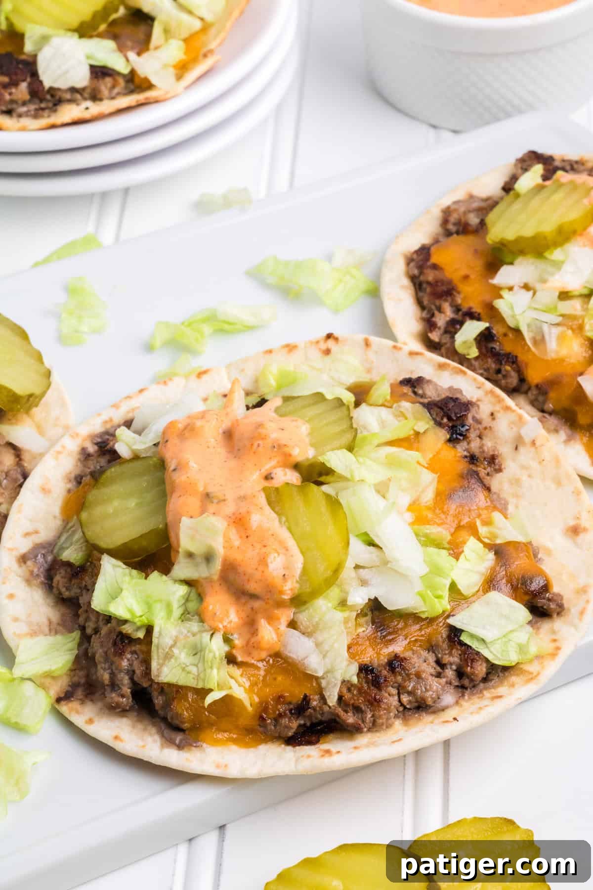 A serving platter showcasing several perfectly assembled Smash Big Mac Tacos, complete with secret sauce drizzled over the top, ready to enjoy.