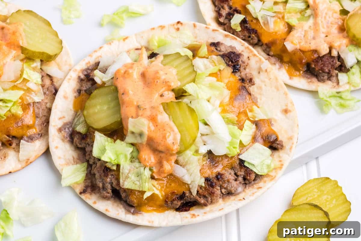 A close-up of a perfectly prepared smash burger taco, Big Mac style, featuring crisp lettuce, dill pickle slices, and a generous drizzle of homemade Big Mac sauce.