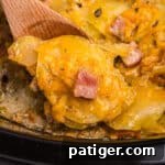 A spoonful of scalloped potatoes and ham being scooped from the slow cooker.