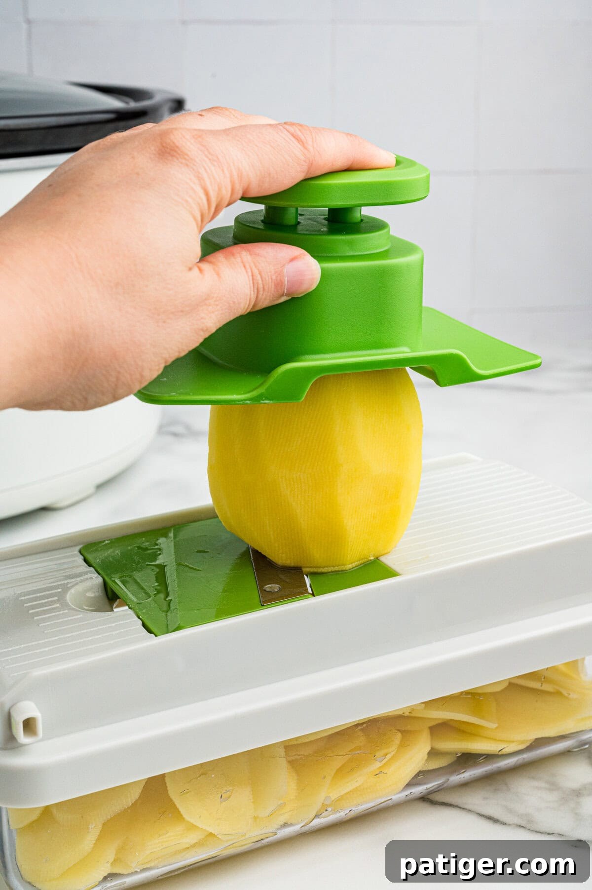 Potato being sliced with mandolin.