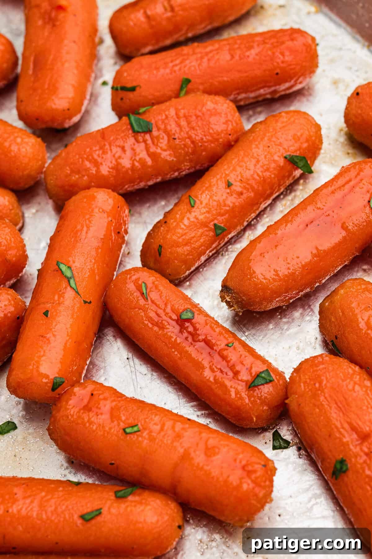 Brown sugar honey glazed carrots beautifully arranged on a metal sheet pan, showcasing their glistening glaze and perfectly caramelized edges.