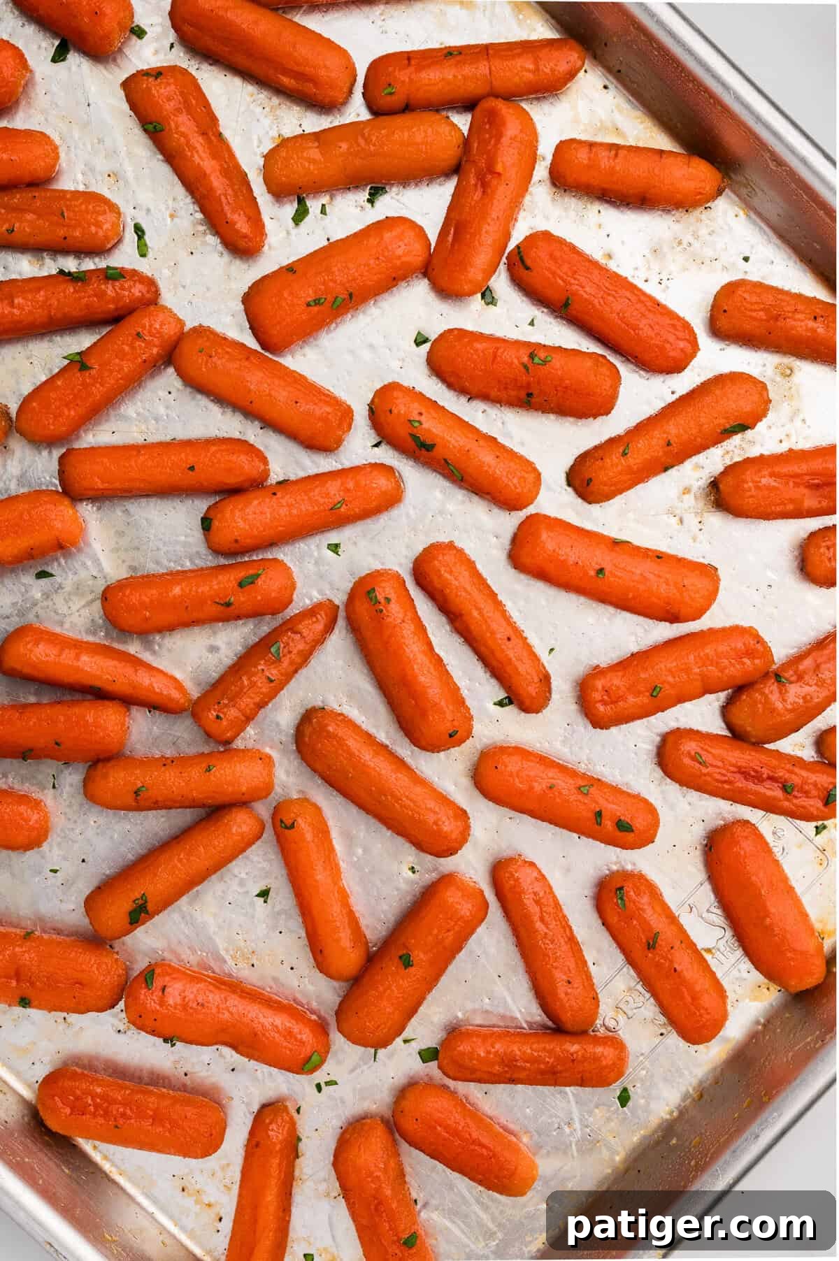 A sheet pan filled with a single layer of glistening roasted baby carrots, beautifully coated in a rich brown sugar honey glaze, fresh out of the oven and ready to serve.