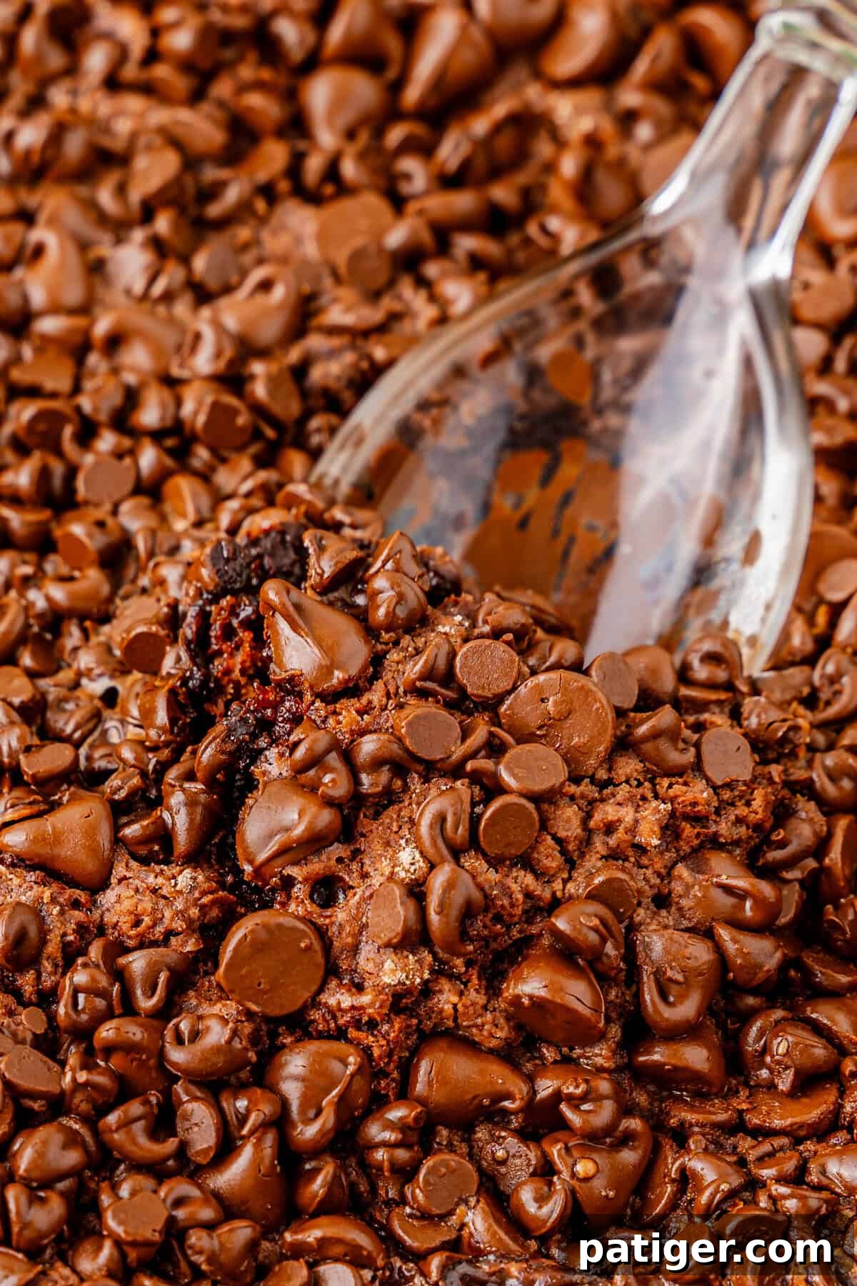 A close-up view of a spoon scooping into freshly baked chocolate dump cake, revealing its soft, gooey texture beneath a generous layer of melted semi-sweet chocolate chips.
