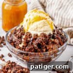 Bowl of chocolate dump cake with chocolate chips, chocolate syrup, and scoop of vanilla ice cream.