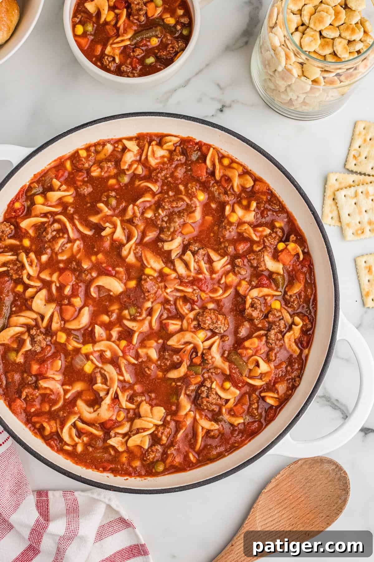 Overhead view of a large pot of hamburger noodle soup with ground beef, egg noodles, vegetables, and a tomato-based broth, ready to be served.