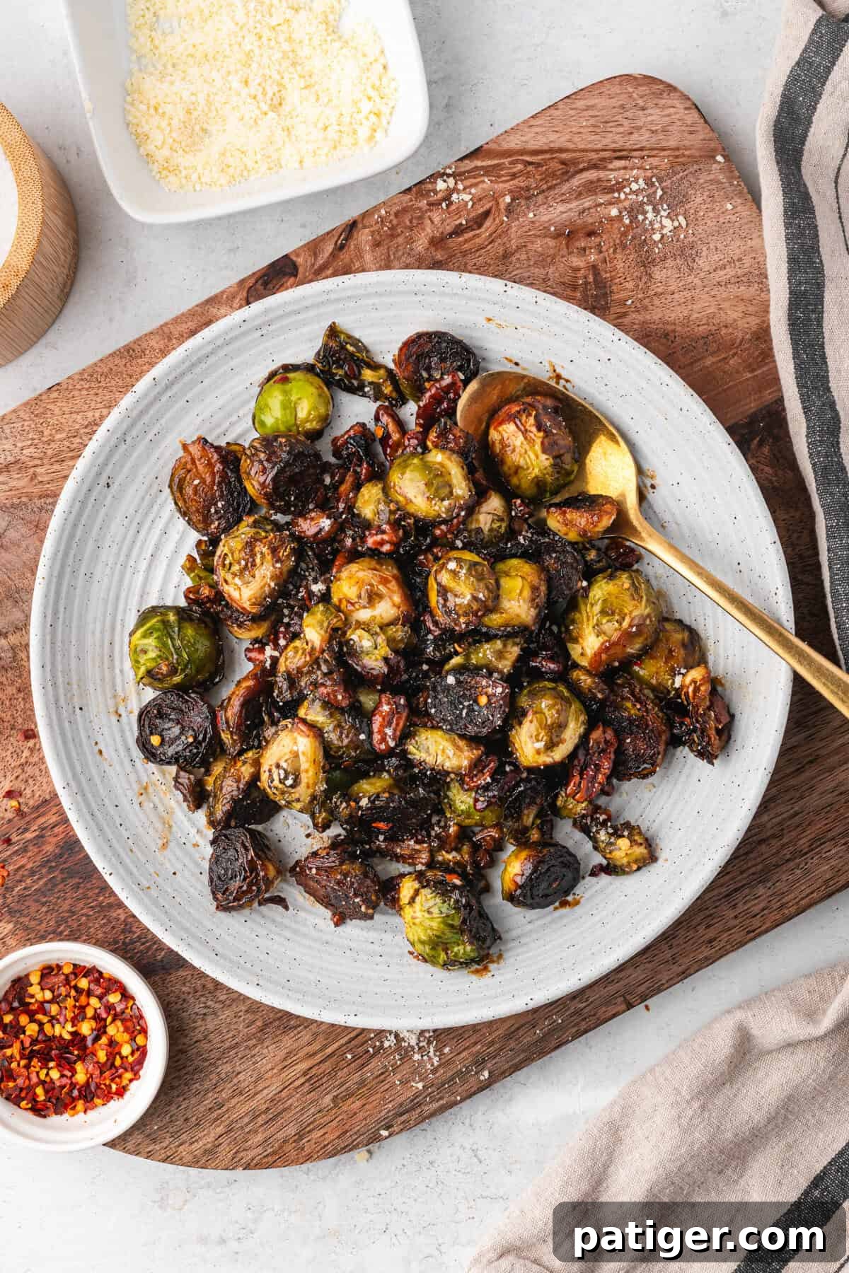 A plate filled with caramelized Brussels sprouts and pecans, sprinkled with seasoning. A gold spoon rests in the dish.