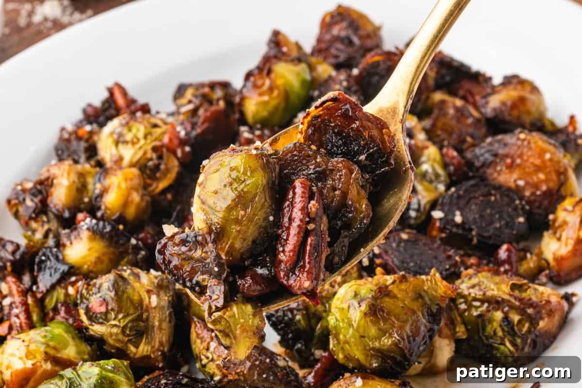 Golden spoon lifting a serving of caramelized Brussels sprouts and pecans, coated in a glossy glaze. The plate beneath is full of additional roasted sprouts and darkened bits from caramelization.