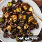 A plate filled with caramelized Brussels sprouts and pecans, sprinkled with seasoning. A gold spoon rests in the dish.