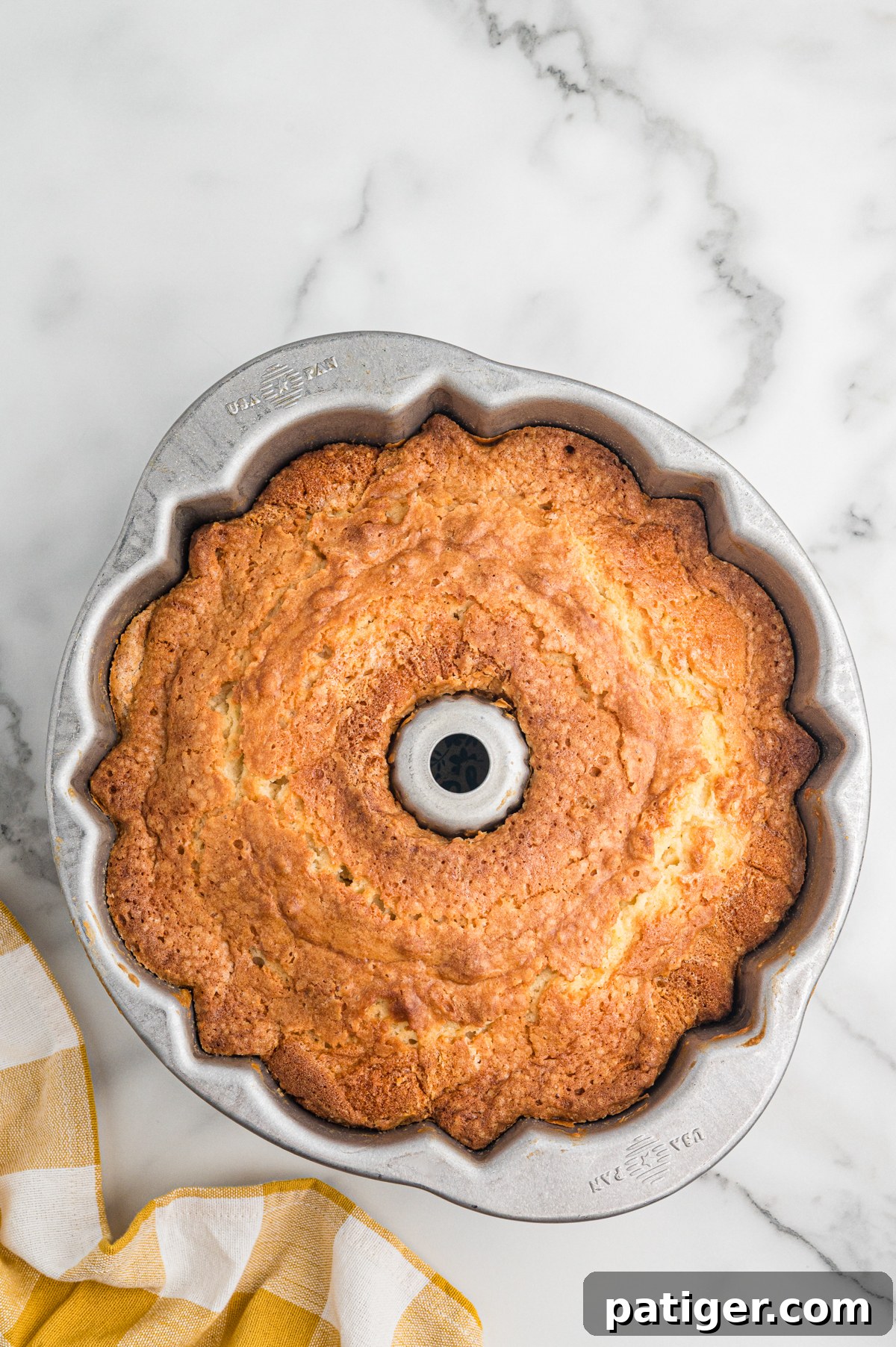 Fully baked 7 Up pound cake with a golden brown crust rests in a silver fluted Bundt pan on a marble surface. The top is domed and lightly cracked.