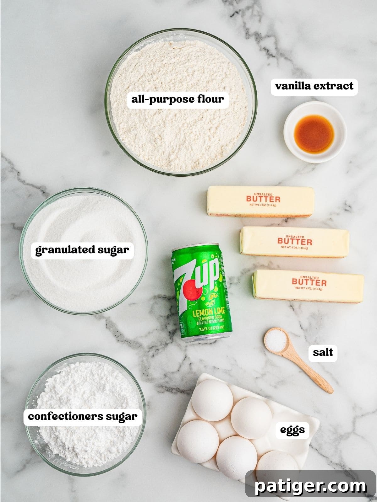 Labeled ingredients for 7 Up pound cake including: bowls of all-purpose flour, granulated sugar, confectioners sugar, and vanilla extract; a small wooden spoon of salt; six eggs in a carton; two sticks of unsalted butter; and a can of 7 Up.