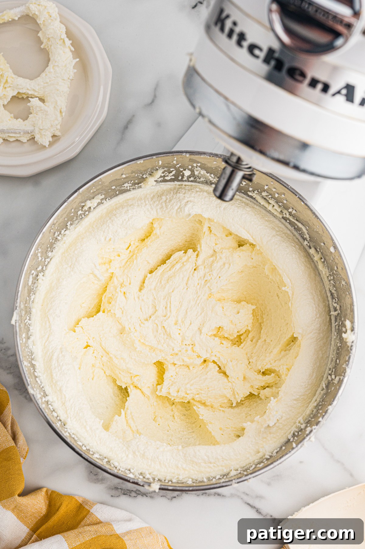 A fluffy, pale yellow mixture of creamed butter and sugar fills a metal bowl attached to a stand mixer.