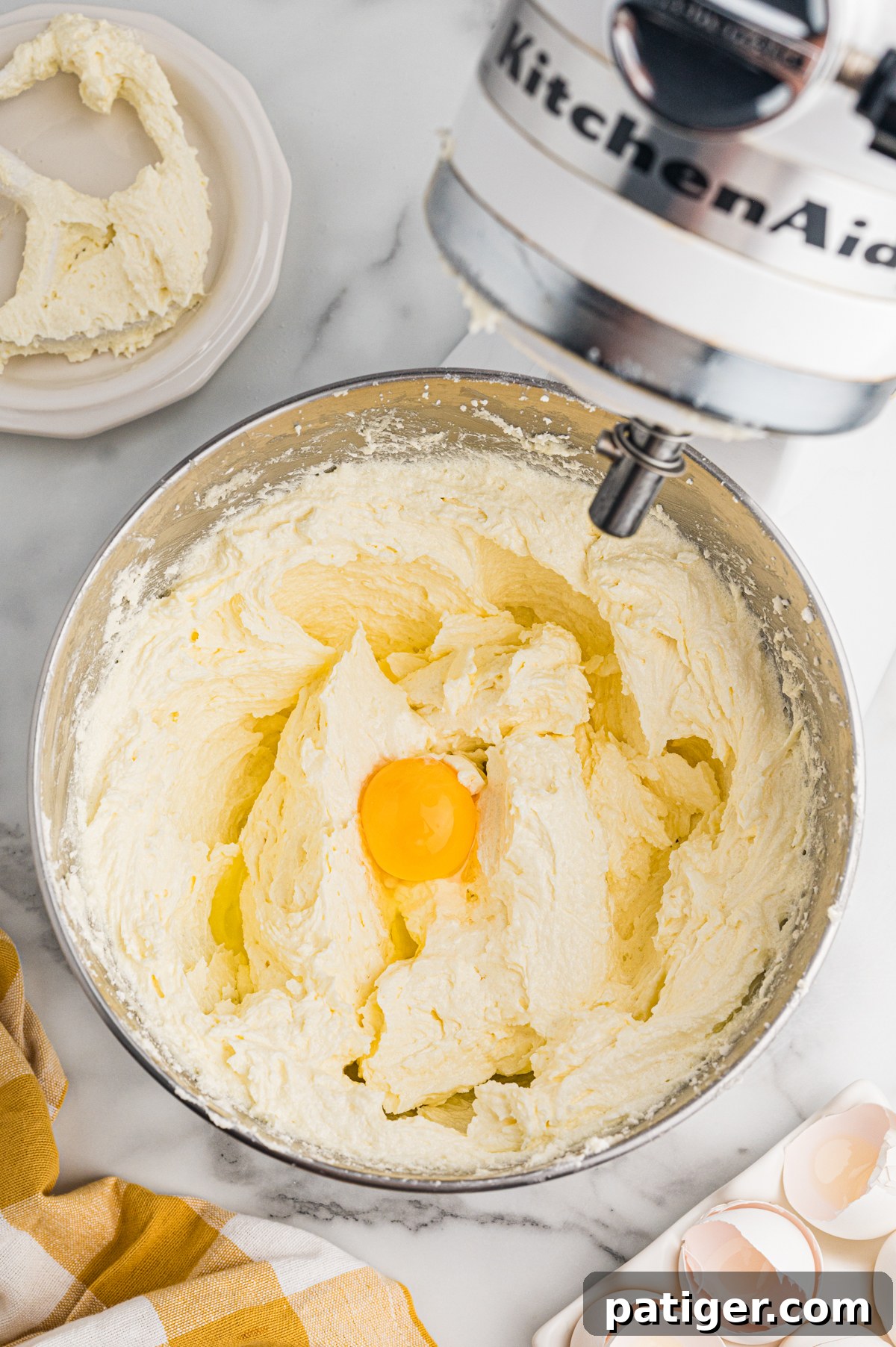 Raw egg added to creamy cake batter in stand mixer bowl.