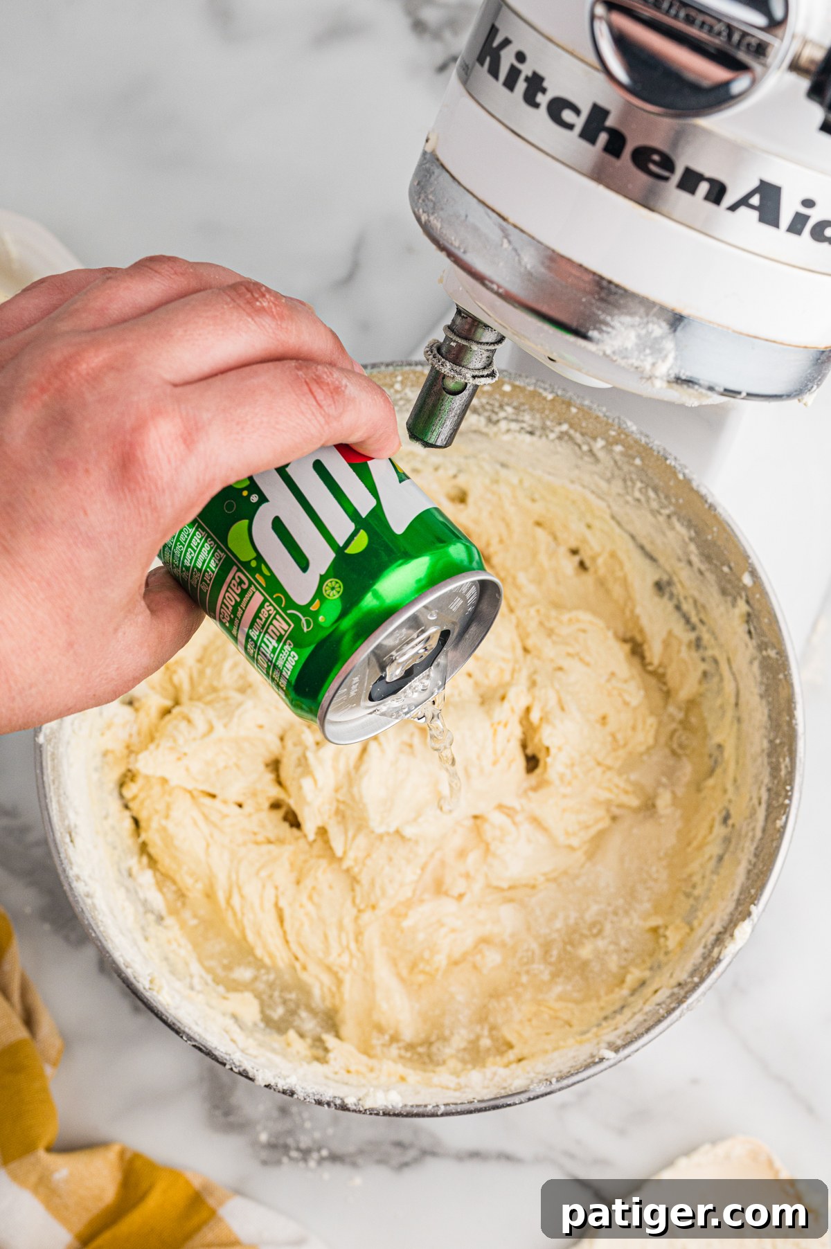 Hand pouring 7 Up into cake batter in mixer bowl.