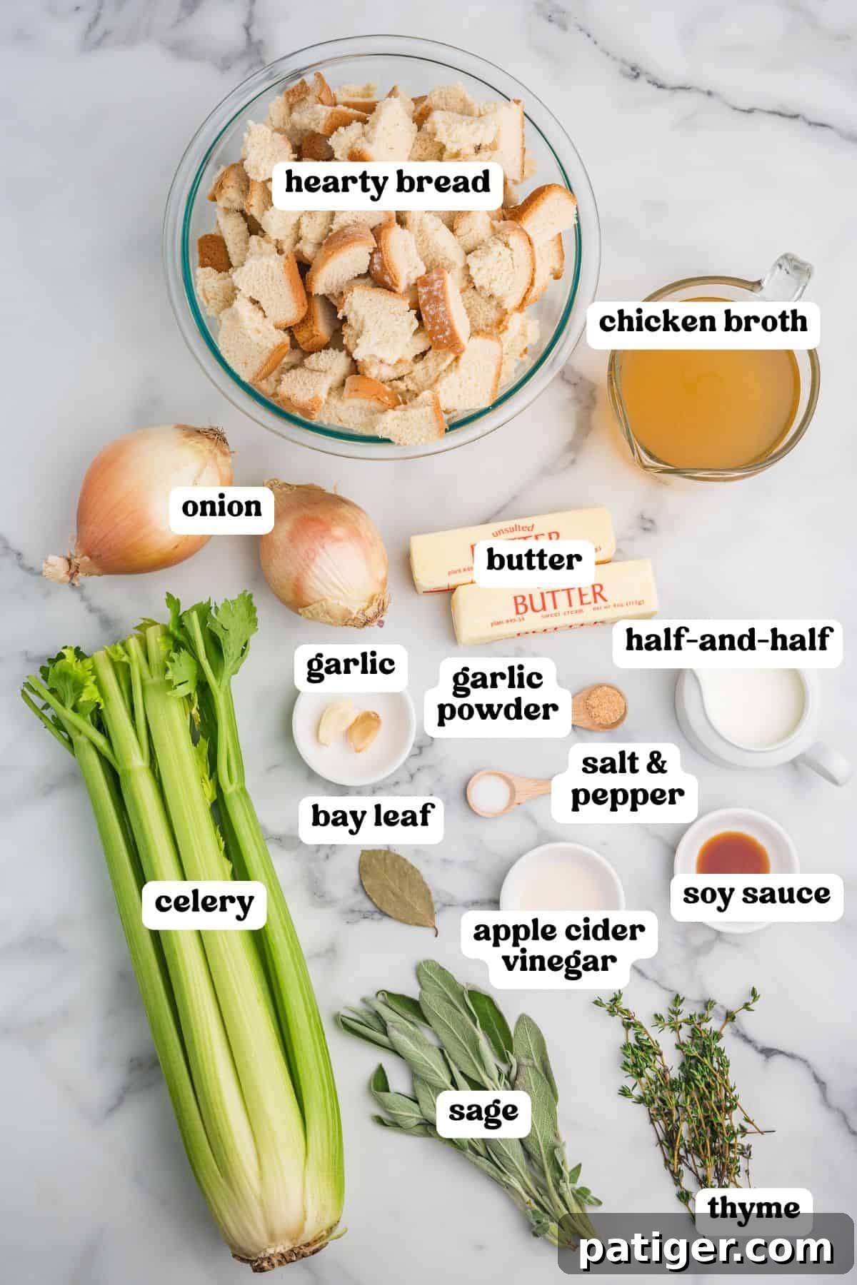 Homemade stuffing ingredients labeled on a marble surface. Visible items include a bowl of torn hearty bread, chicken broth, onions, celery, garlic, bay leaf, butter, half-and-half, garlic powder, salt and pepper, soy sauce, apple cider vinegar, fresh sage, and thyme.