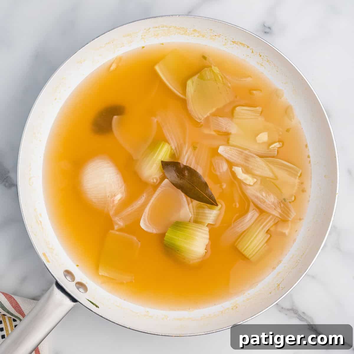 Pan of broth with onions, celery, and bay leaves.