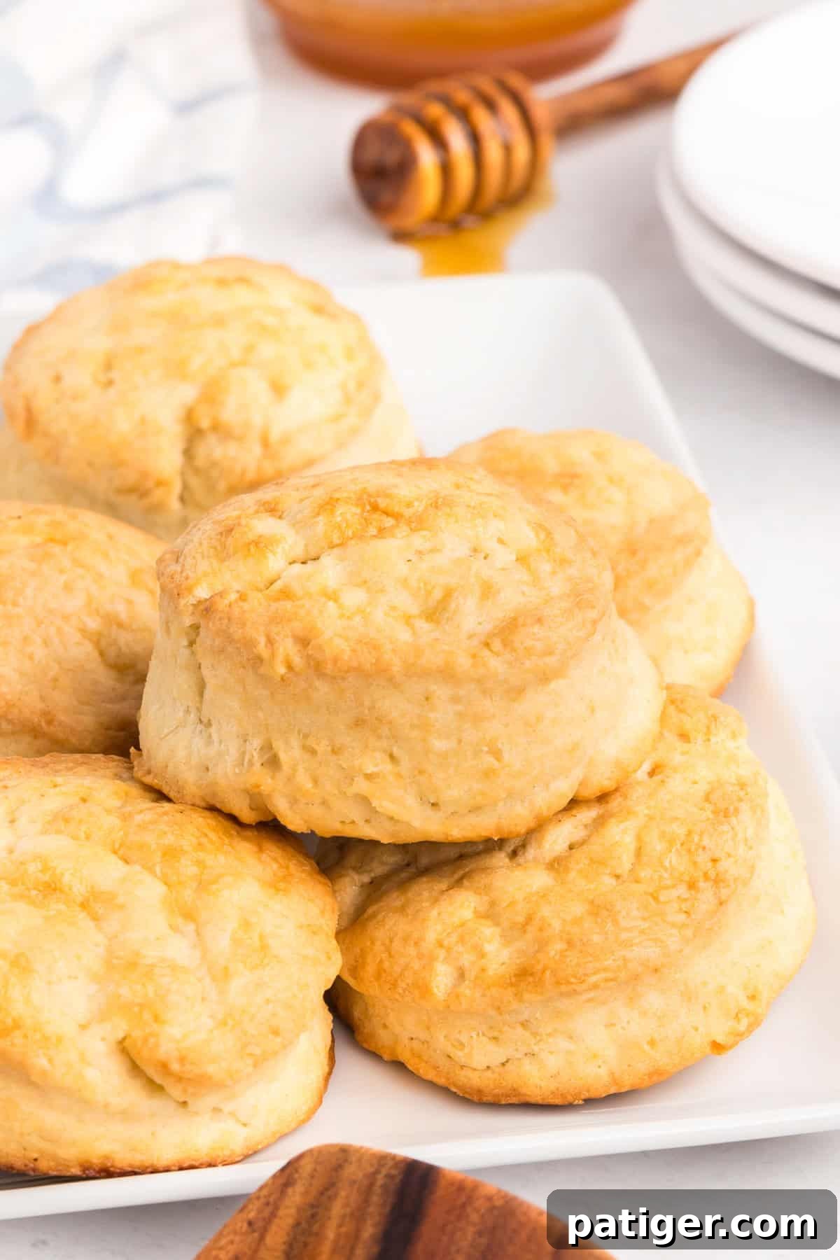 Close-up of several golden brown, fluffy biscuits stacked on a white plate, showing crisp edges and soft texture.