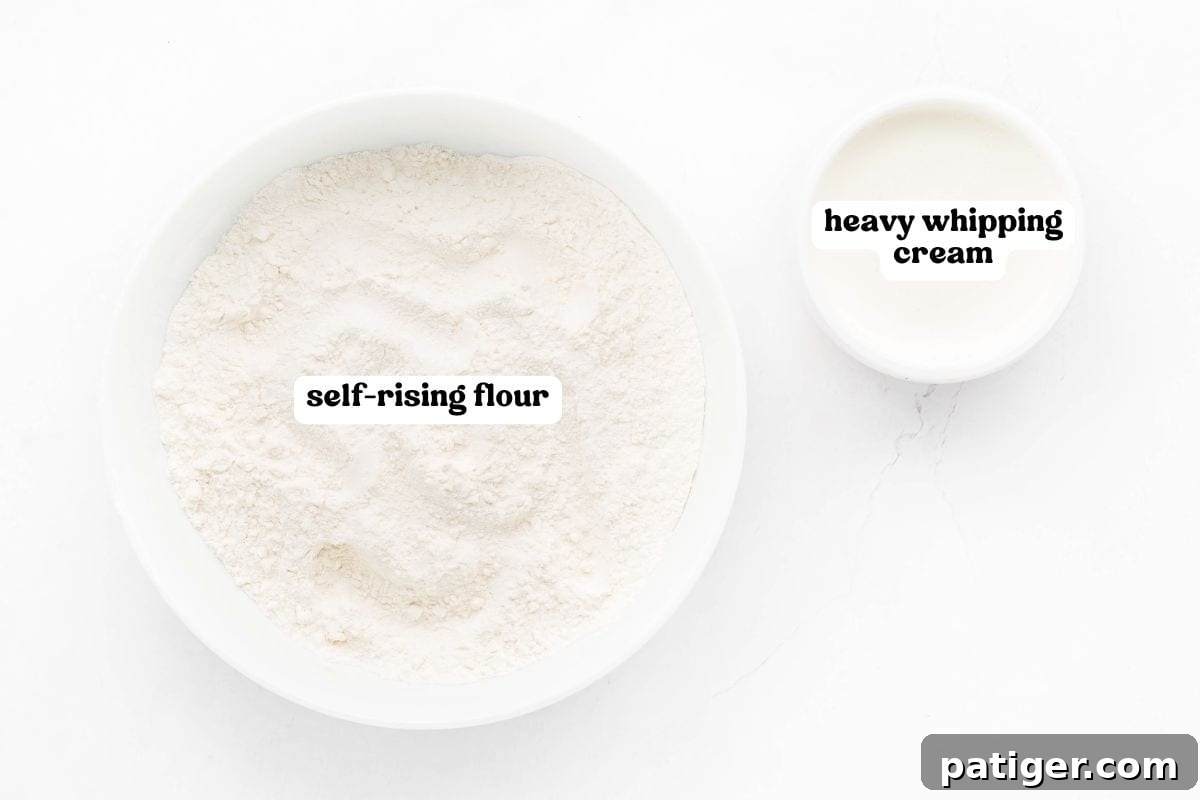Overhead image of two white bowls on a light surface—one large bowl filled with self-rising flour and one smaller bowl with heavy whipping cream. Both bowls are clearly labeled with bold black text.