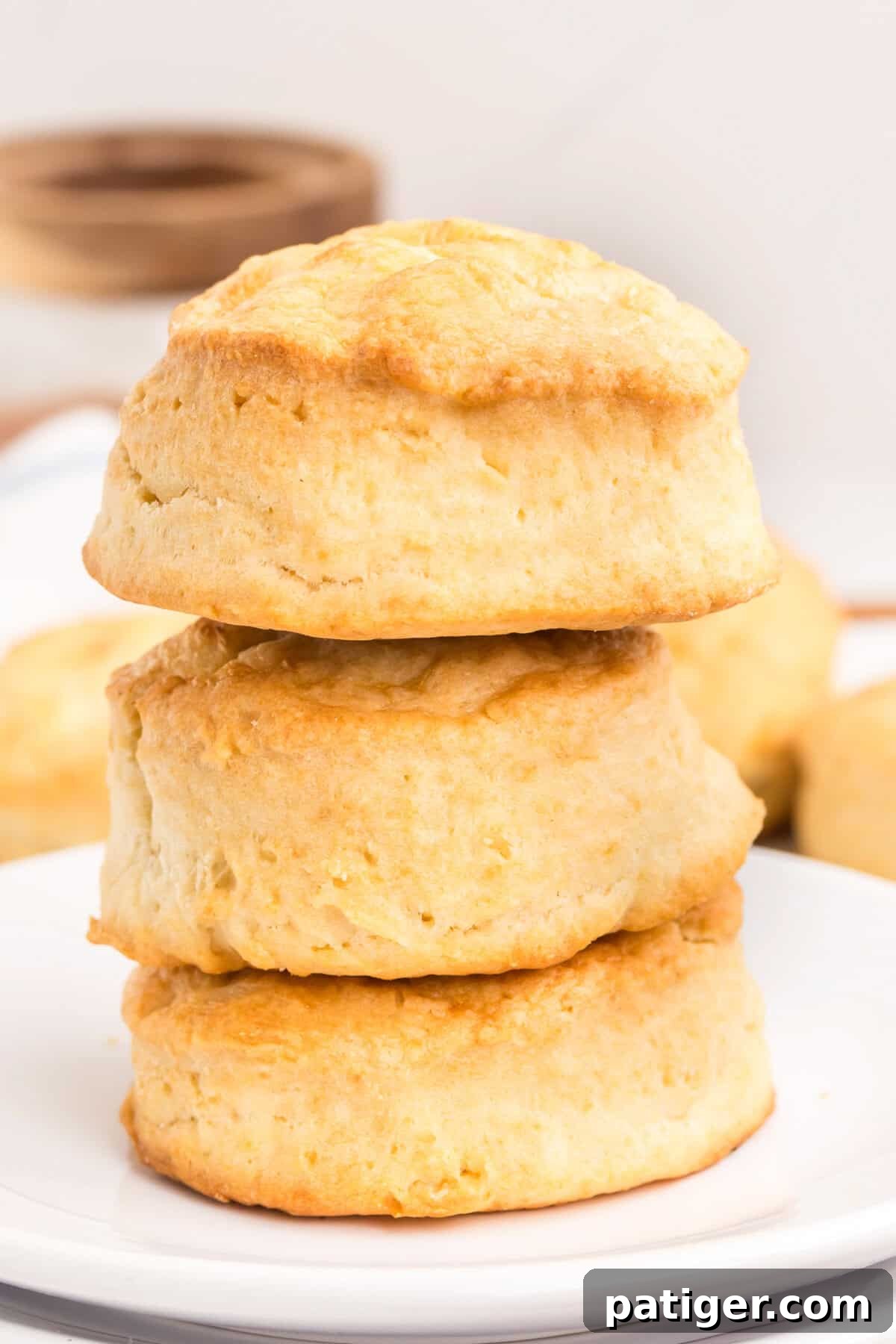Three golden, fluffy biscuits stacked vertically on a white plate.