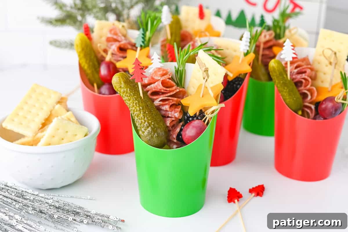 A pair of beautifully arranged Christmas charcuterie cups in red and green paper, each overflowing with folded salami skewers, star-shaped cheddar cheese, succulent grapes, tangy gherkins, crisp crackers, and fragrant rosemary sprigs, perfectly showcasing their festive appeal.