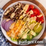 Top-down view of a burger bowl with seasoned ground beef, pickles, cheese, tomato, onion, and a drizzle of homemade burger sauce.